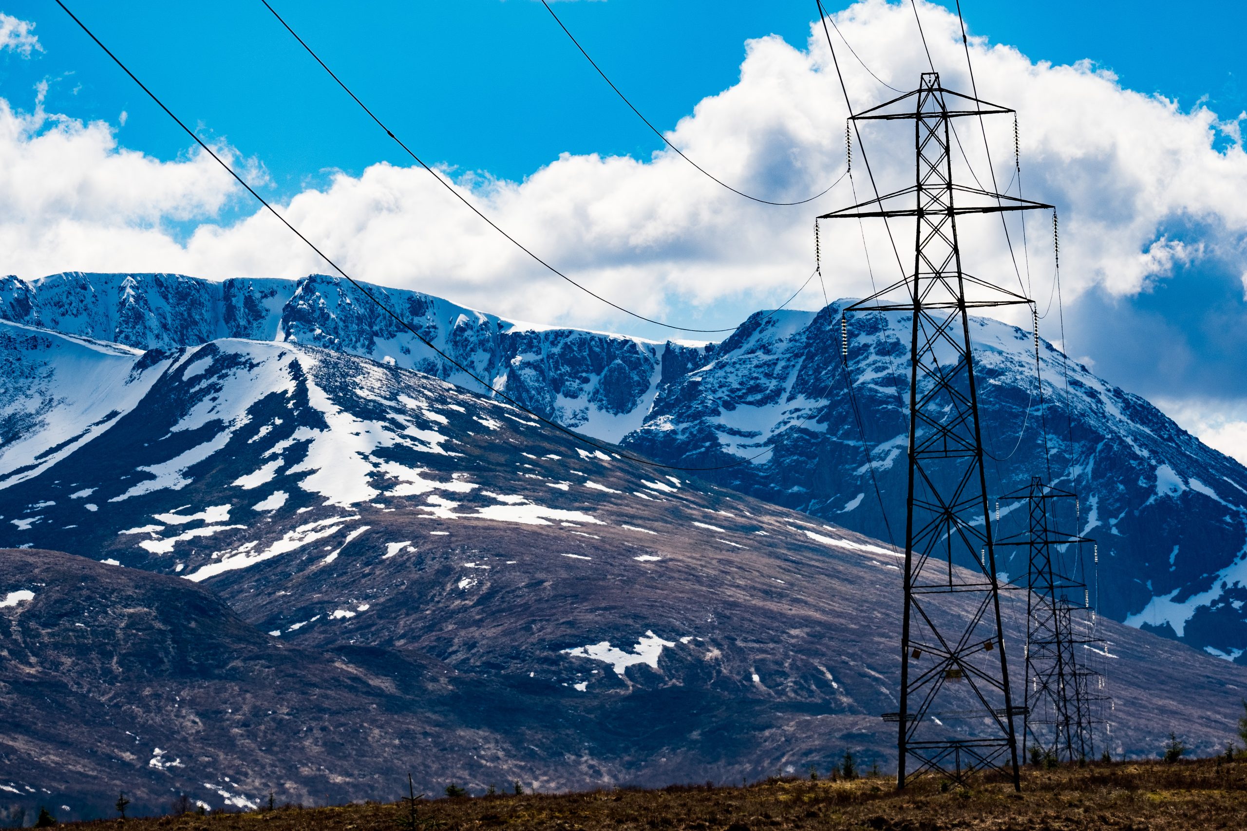 Snow capped hills wiht clear blue skies and electrcicity pylons dotted across the lanndscape.